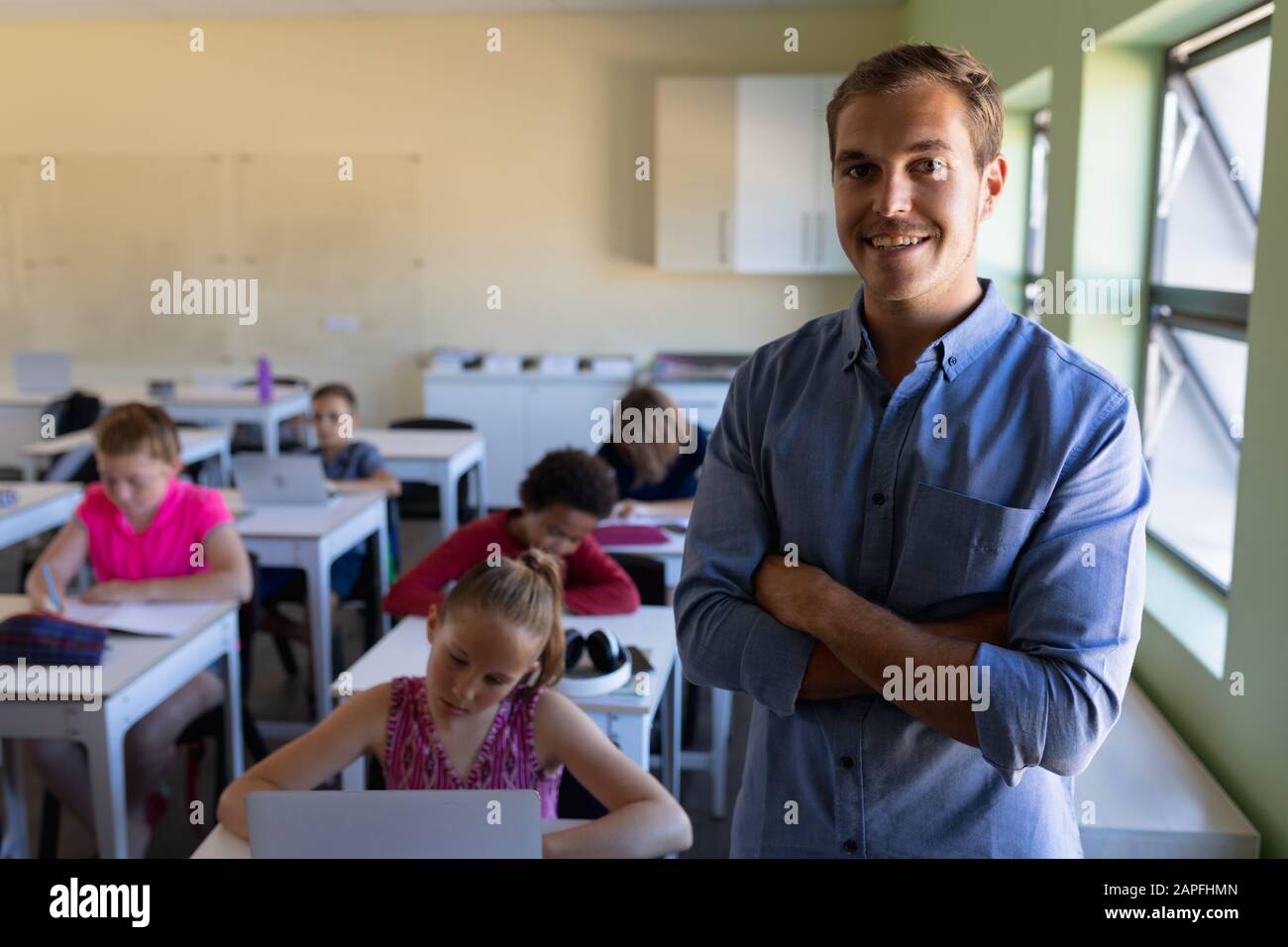 Male school teacher standing with arms crossed in an elementary school classroom Stock Photo