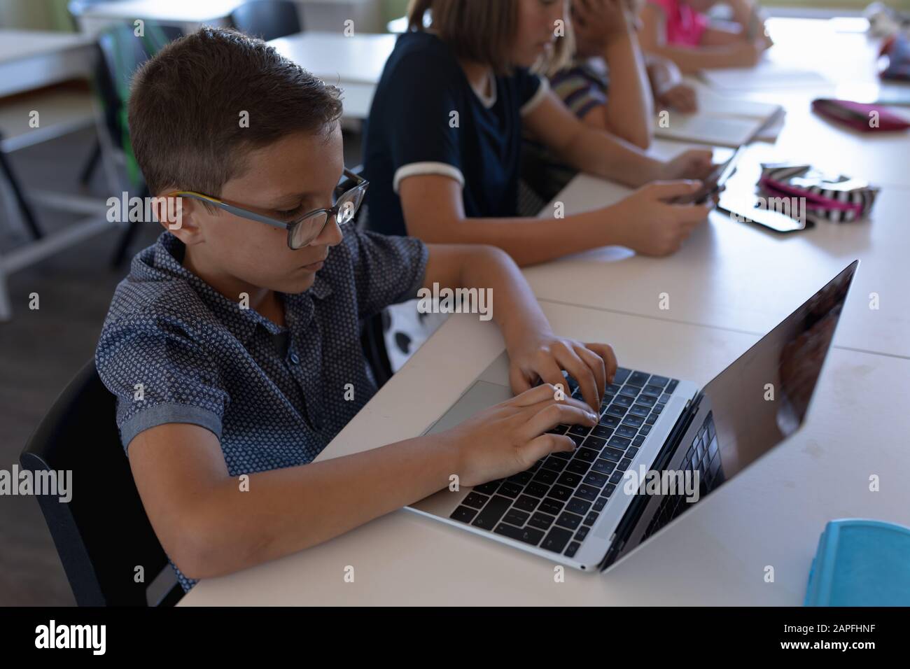 Schoolboy wearing glasses sitting at a desk using a laptop computer Stock Photo