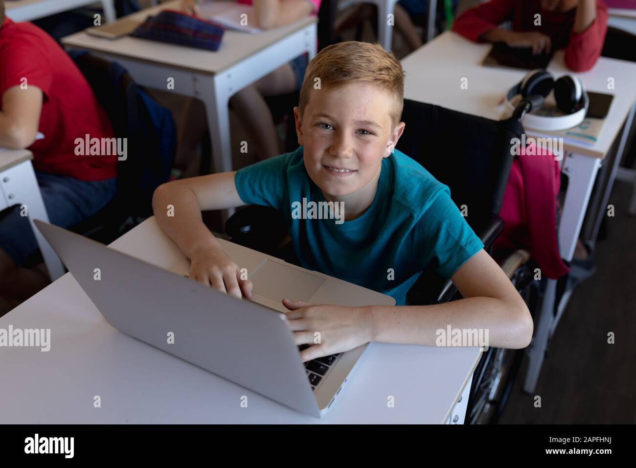 Schoolboy wearing glasses sitting at a desk using a laptop computer ...