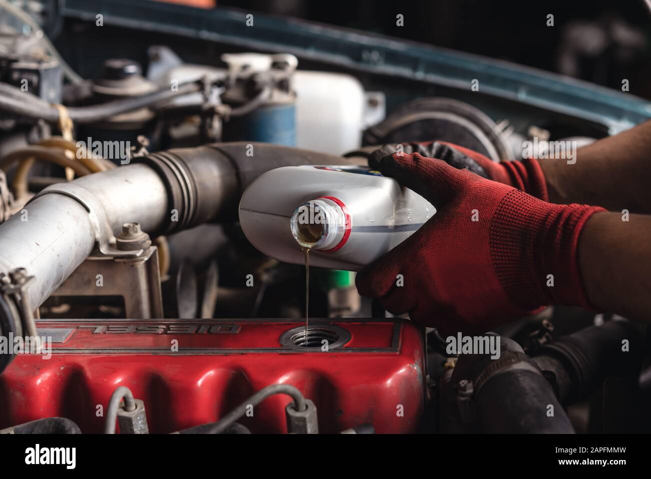 Hands of auto repair mechanic filling lubricant oil in engine of car during service - Vehicle maintenance technician carrying out annual servicing inspection - Garage, industry and mechanical concept Stock Photo