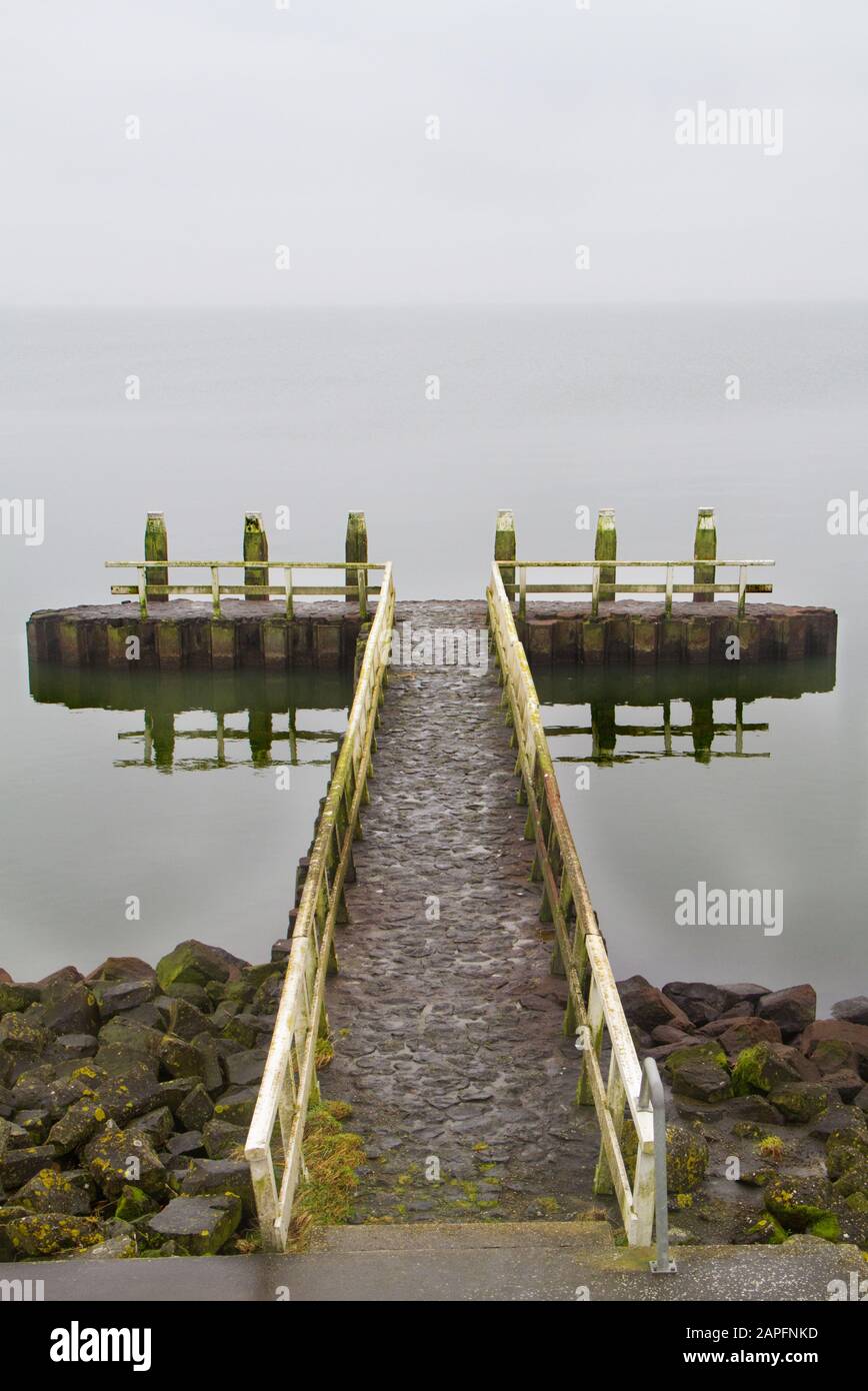 Pier with landing stage at Afsluitdijk in the Netherlands on a grey, misty day Stock Photo