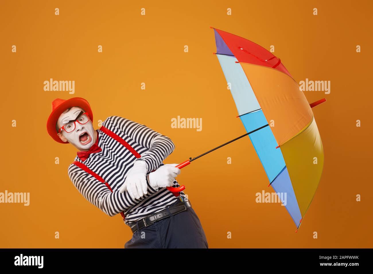 Mime with multi-colored umbrella isolated on blank orange background in studio Stock Photo