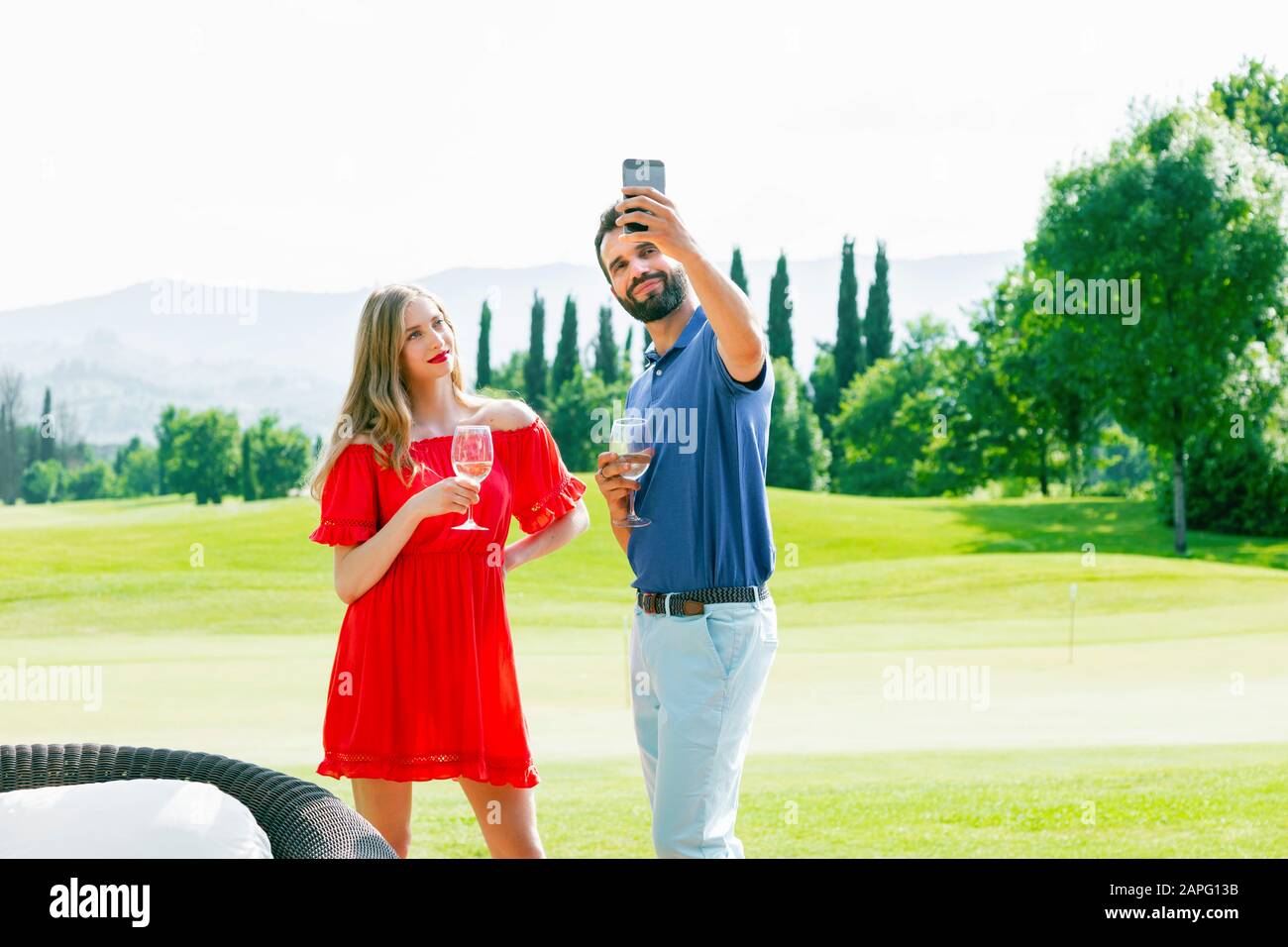 Couple with wine glasses taking selfie on golf course Stock Photo