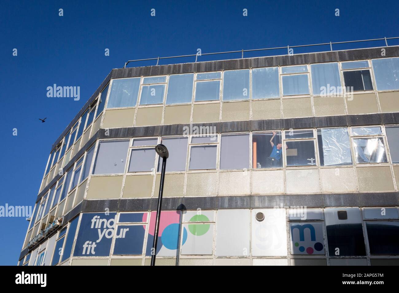 As a bird flies overhead, a workman stretches into the corner of a window of a local gym business, on 21st January 2020, in Croydon, London, England. Stock Photo