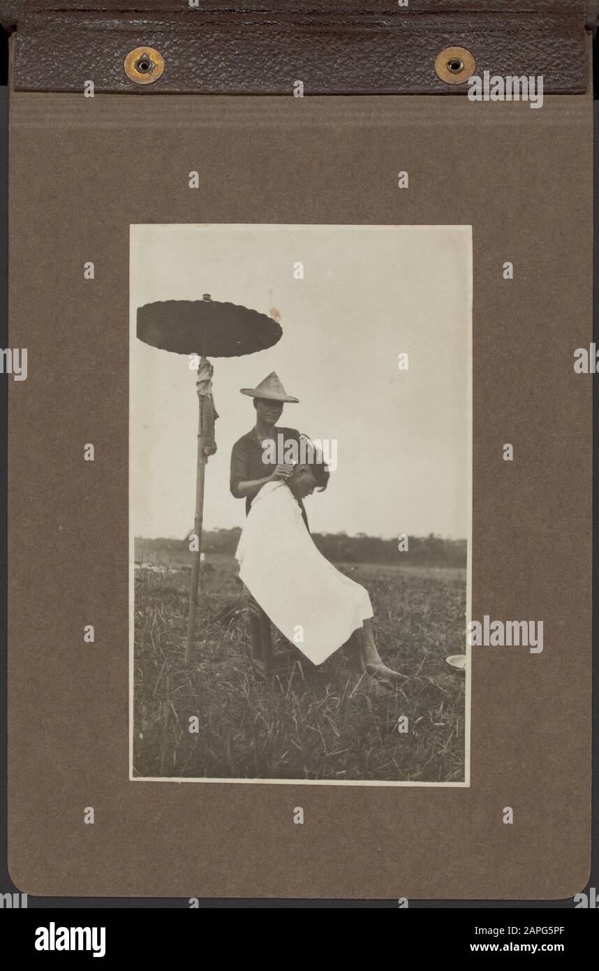 Photo album Deli Maatschappij: A tobacco company in Deli Description: Chinese hairdresser shaves a native worker in the open field under a bamboo parasol Date: 1920 Location: Deli, Indonesia, Dutch- India, Sumatra Keywords: workers, hairdressers, umbrellas, plantations Stock Photo