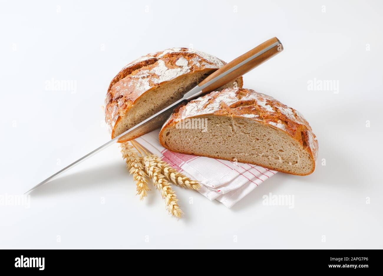 Two halves of a loaf of rustic bread with a knife between them Stock Photo