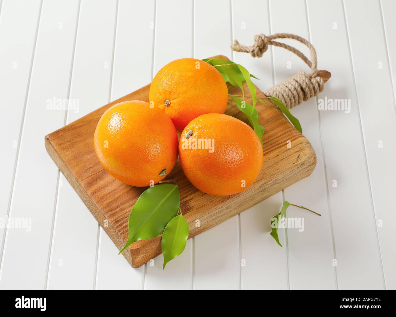 Three whole ripe oranges and leaves on cutting board Stock Photo