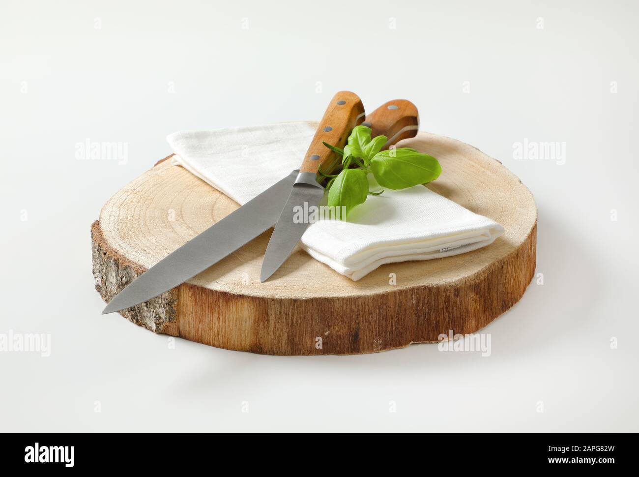 Set of two sharp pointed tip kitchen knives and white napkin on round wood slab Stock Photo