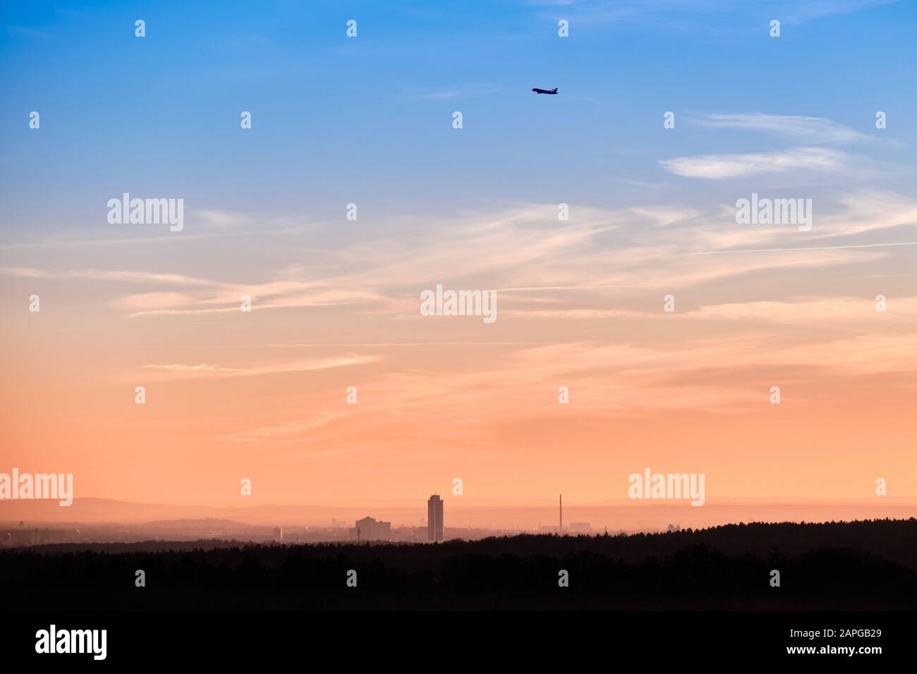 Beautiful sunset landscape with the skyline of Nuremberg and an aeroplane starting into the sky. Seen in Bavaria, Germany in January from Tauchersreut Stock Photo