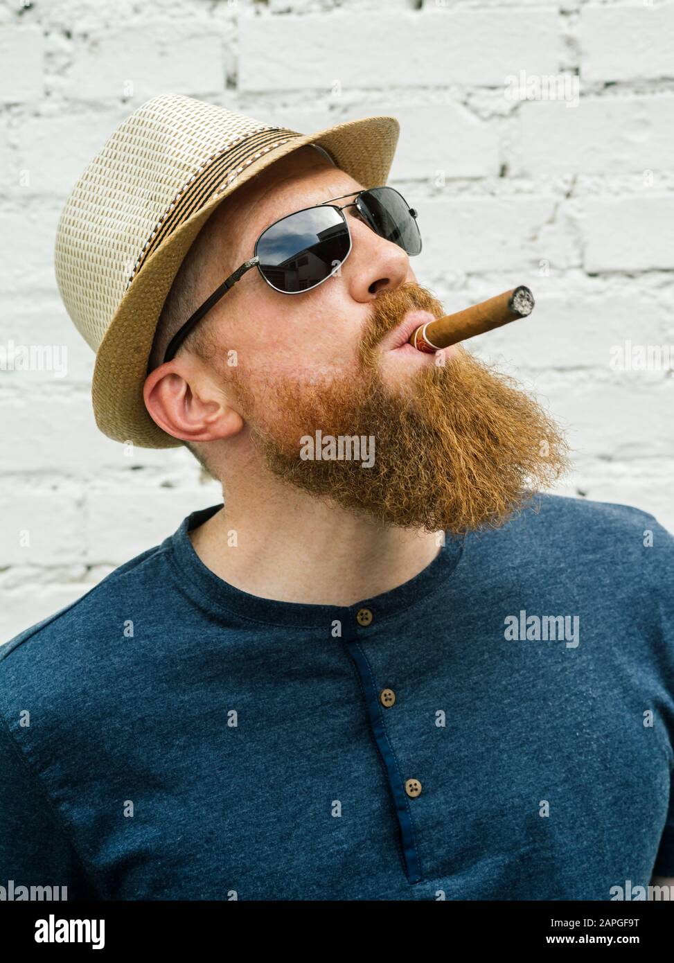 Young adult male wearing fedora and sunglasses smoking a cigar on the street. Stock Photo