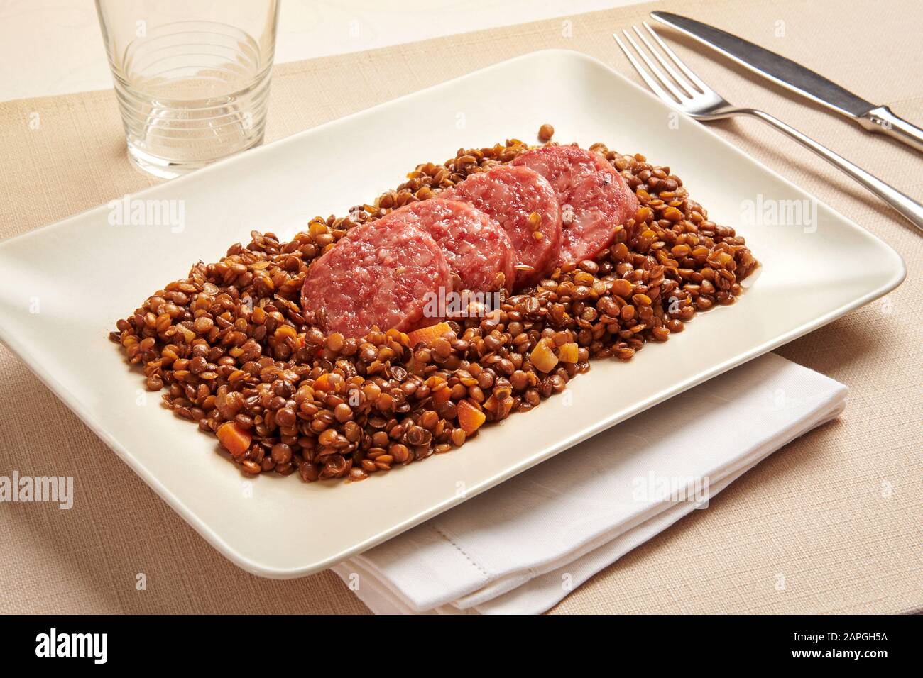Cotechino and lentils, a traditional northern Italian dish of spicy pork sausage and brown lentils served on New Years Eve, on a rectangular platter Stock Photo