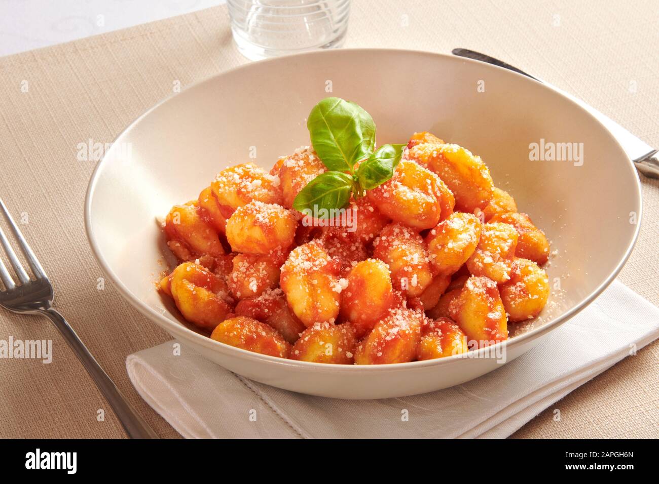 Serving of Italian gnocchi pasta in a bowl with pomodoro sauce and fresh basil on a folded napkin at table, a traditional regional Italian dish Stock Photo