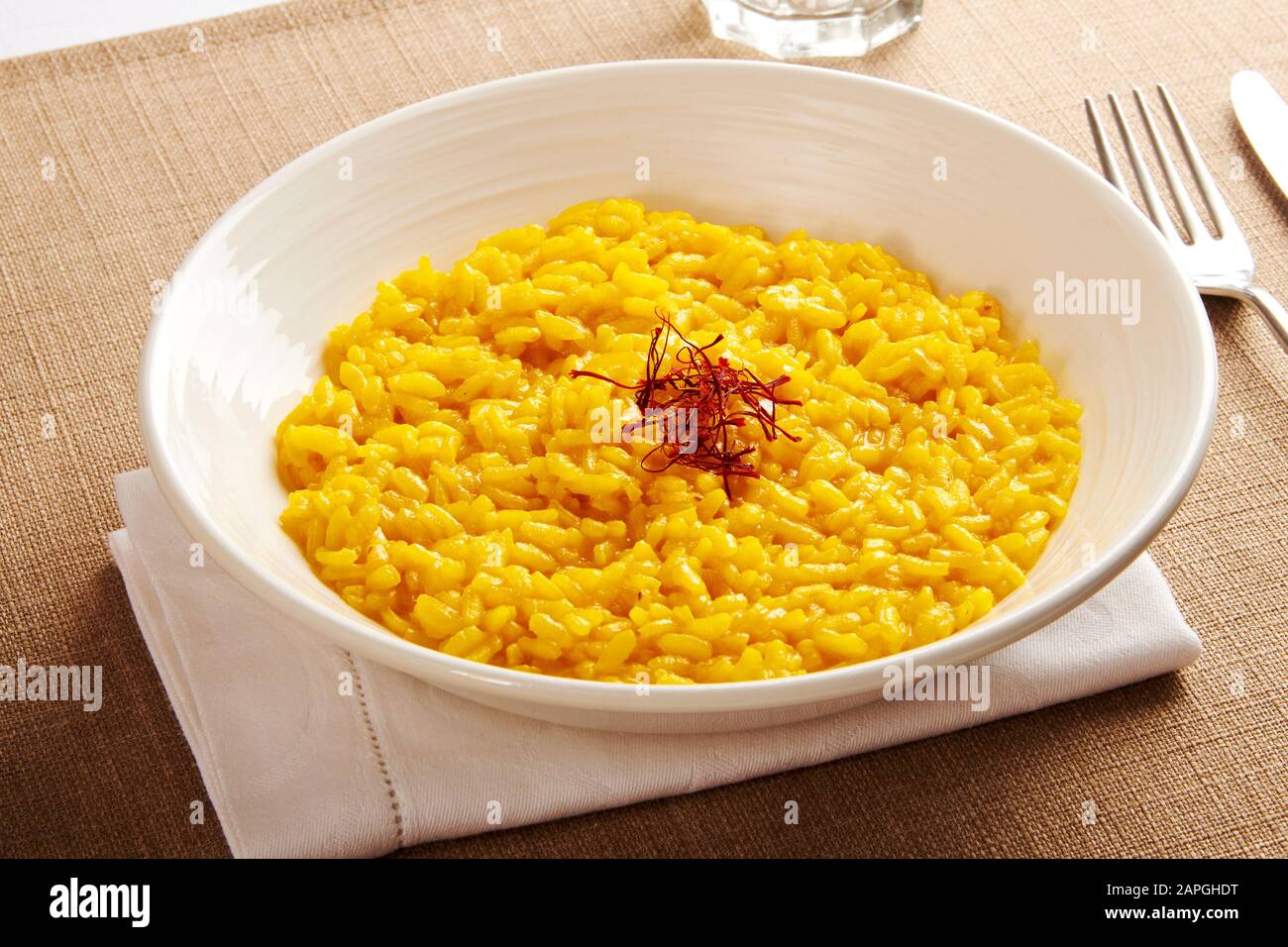 Bowl of creamy yellow risotto rice with saffron threads from the Lombardy region of Italy served in a white bowl at table Stock Photo