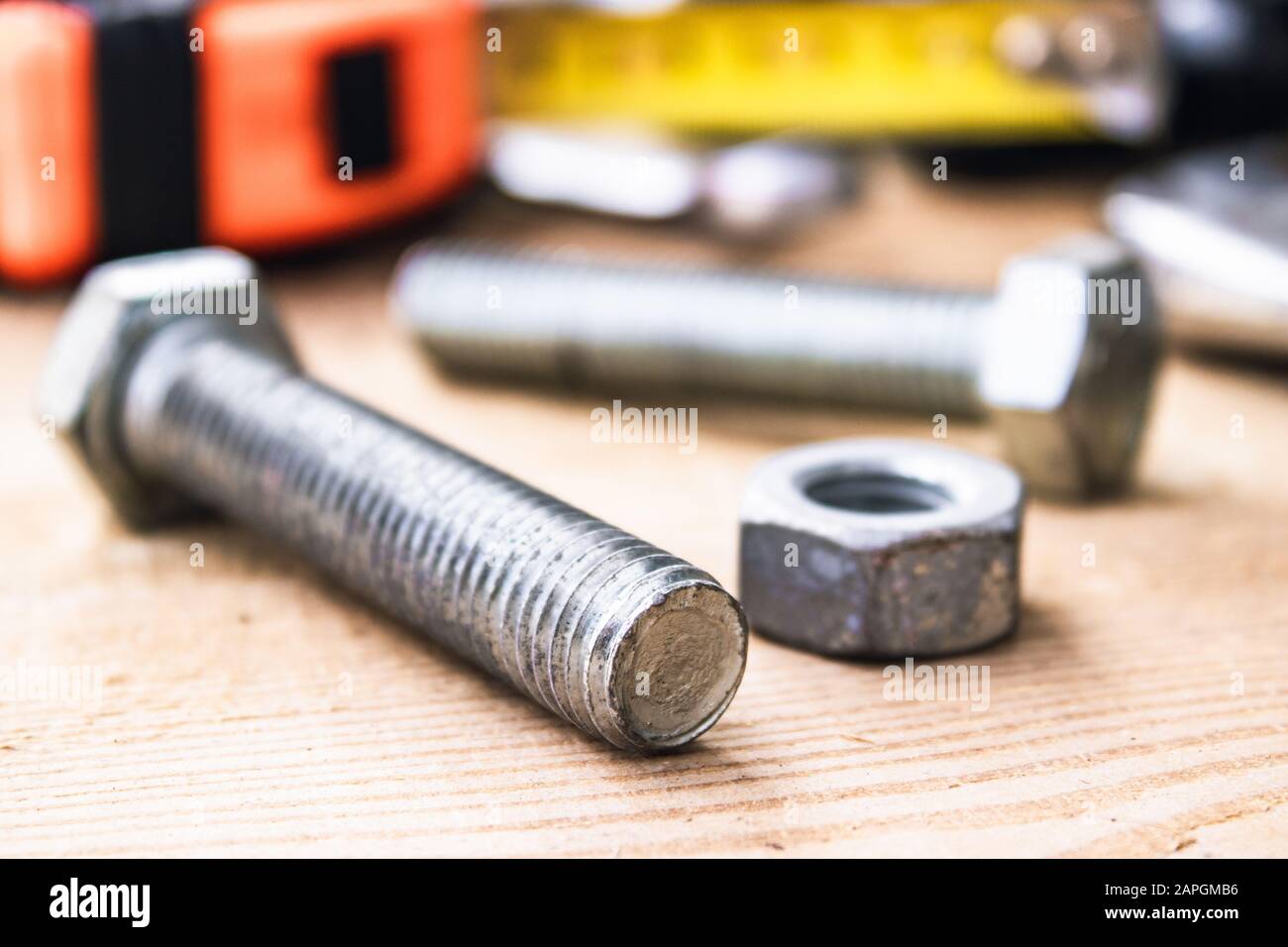 Steel bolt nuts and washers lie on wooden boards near an adjustable spanner and a tape measure