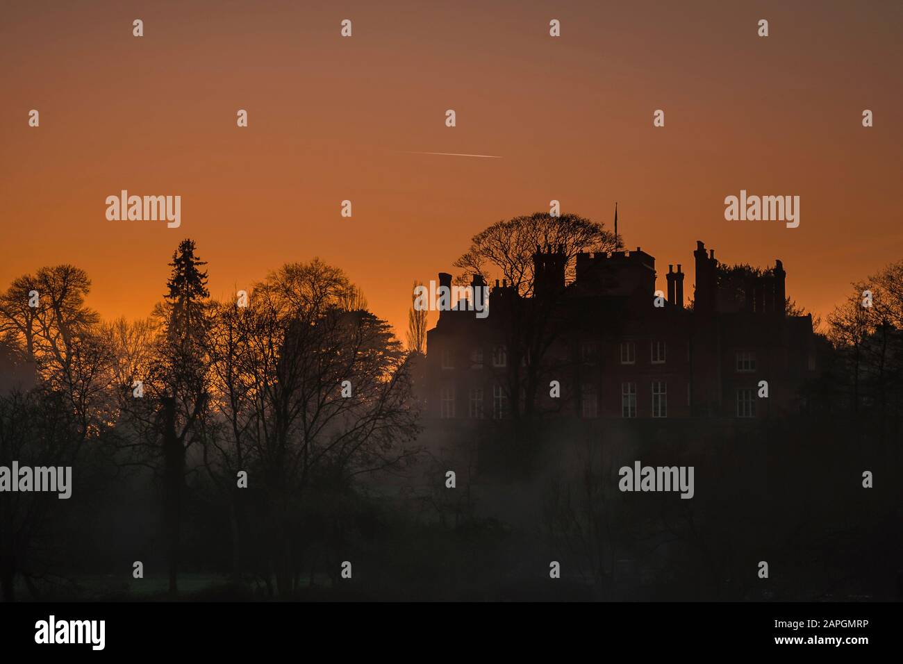 Large UK residential property in silhouette at twilight against an orange, sunset sky in mist. Stock Photo