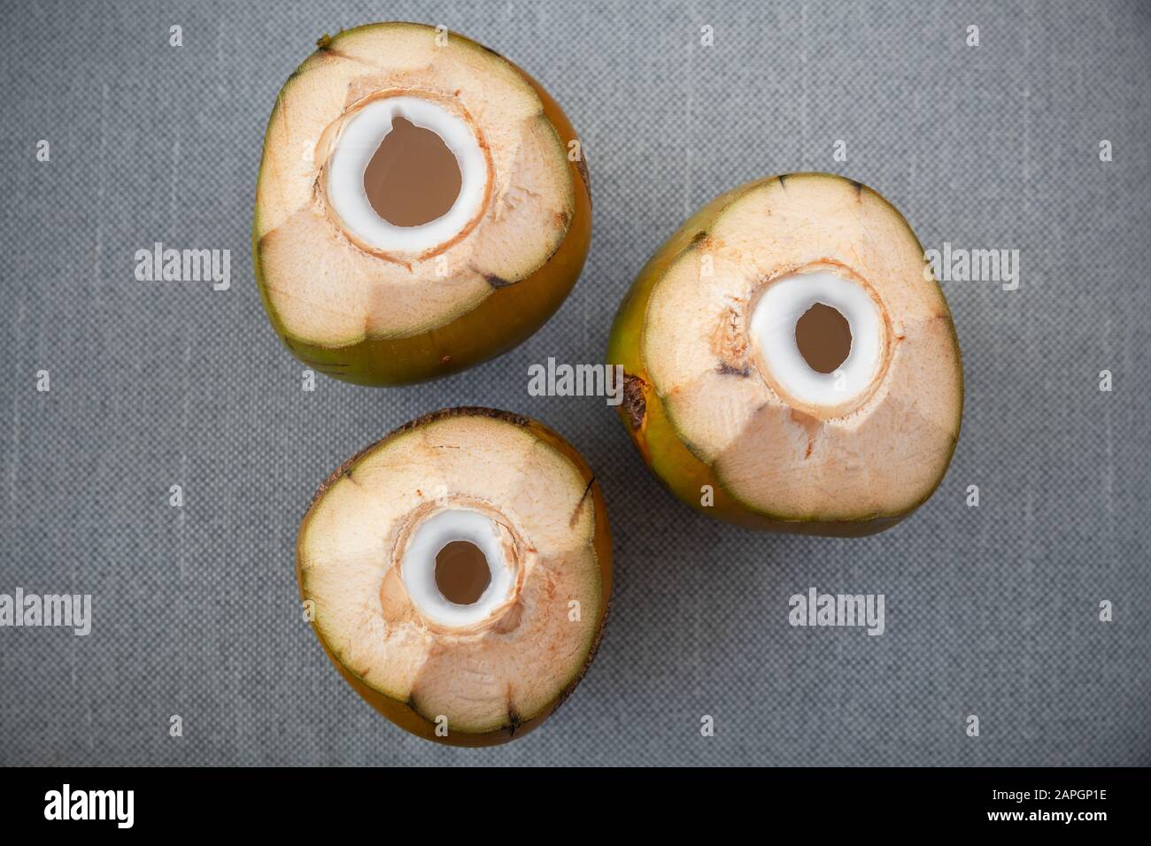 Three juicy green coconuts with holes for straw stand on a gray surface, flat lay photo, top view Stock Photo