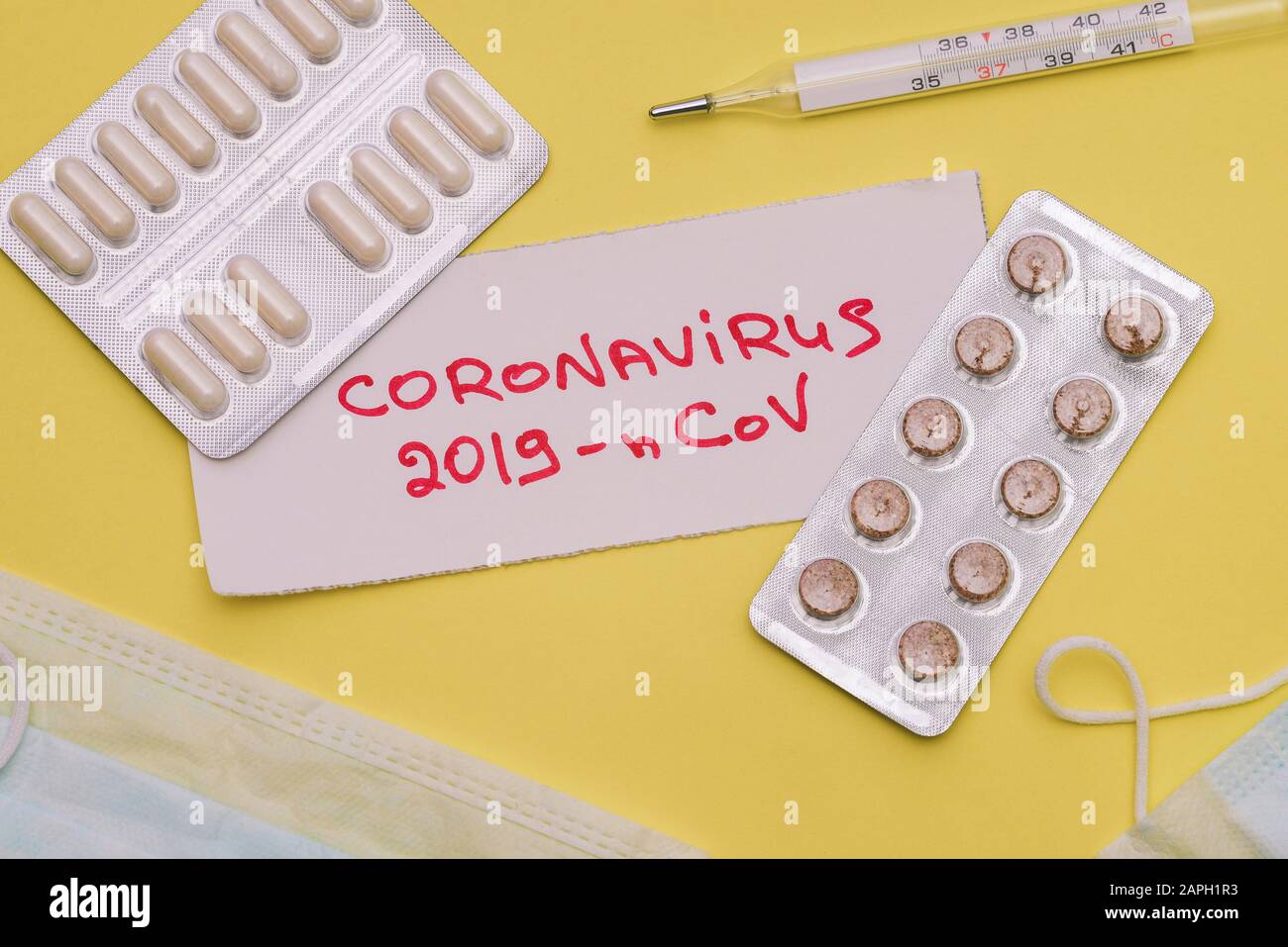 Novel coronavirus 2019-nCoV handwritten text on a yellow background. Virus protection, respiratory mask, pills and thermometer Stock Photo
