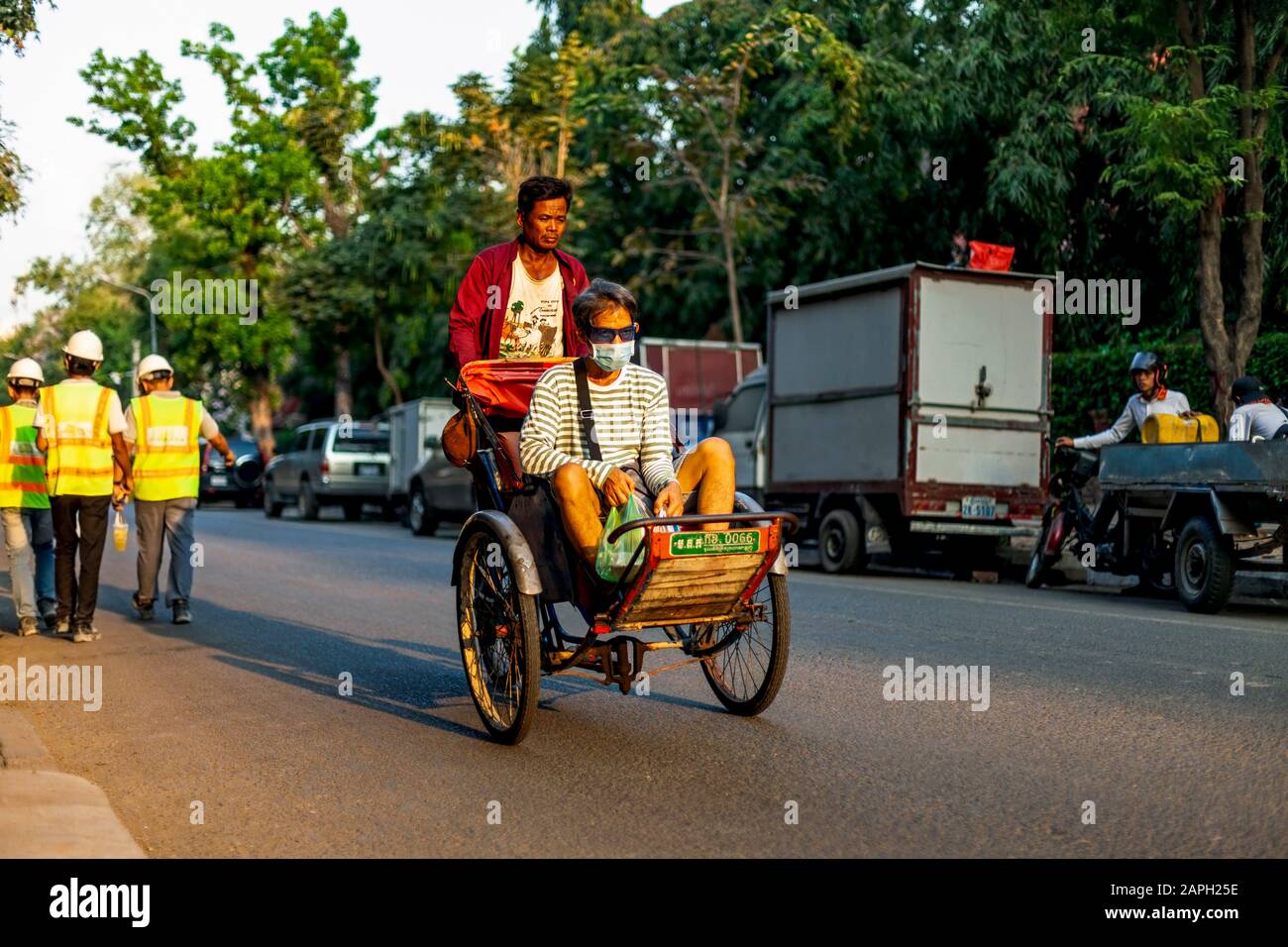 A Khmer cyclo driver is peddling a cyclo while a male passenger sits in the seat on a city street known as art row in urban Phnom Penh, Cambodia. Stock Photo