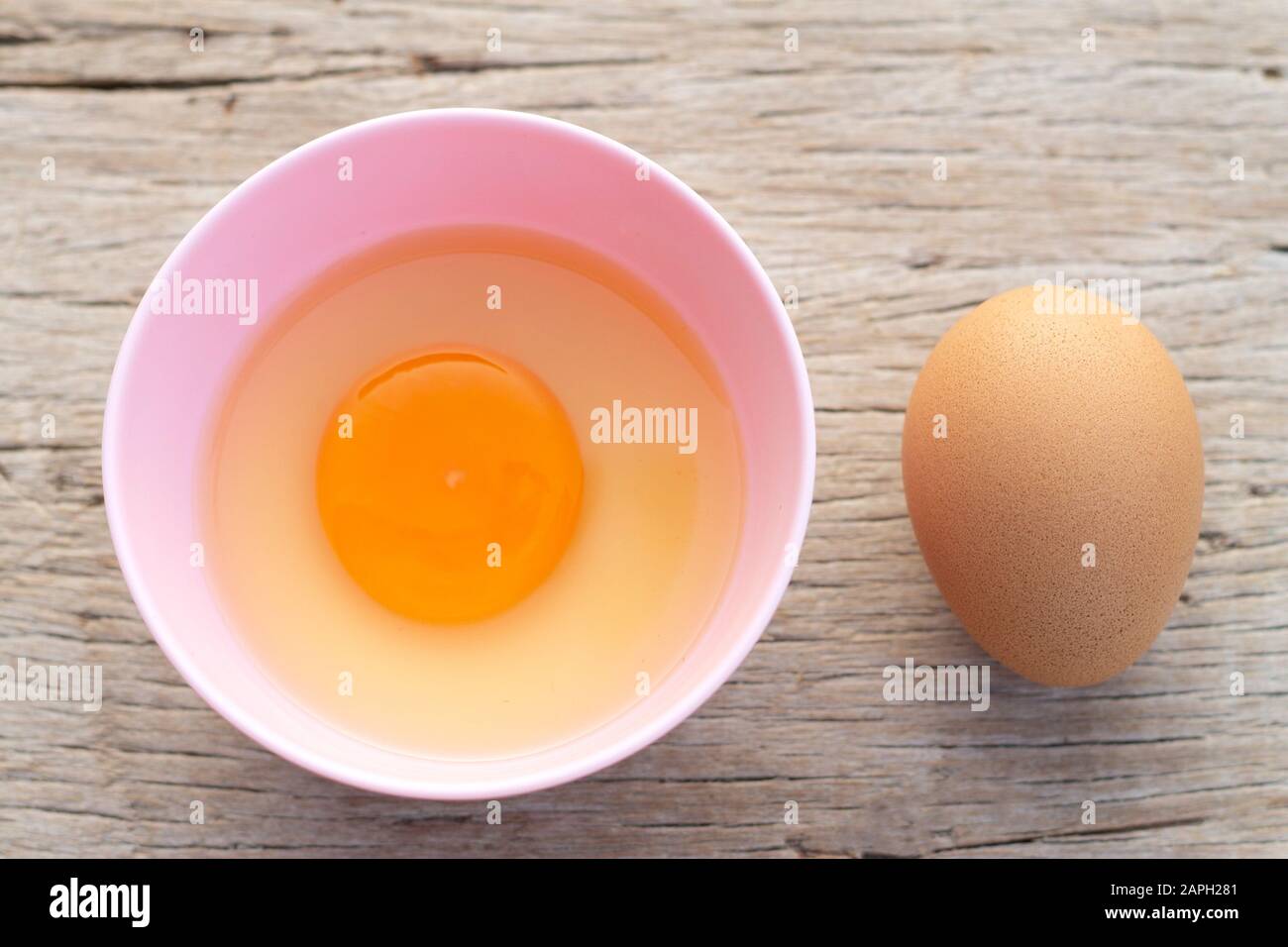 Broken egg shells and raw egg in small bowl  at wooden background for menu and recipe Stock Photo