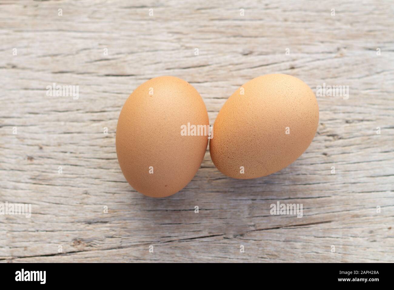Two brown raw chickens eggs are on a wooden background table. Stock Photo