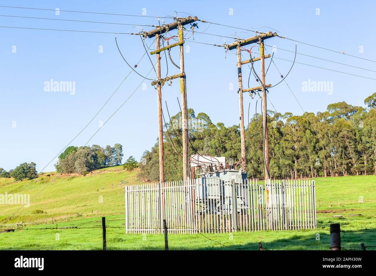 Electricity power transformer unit with secure fencing around unit connectors power lines on wood poles in summer morning rural field farmlands summer Stock Photo