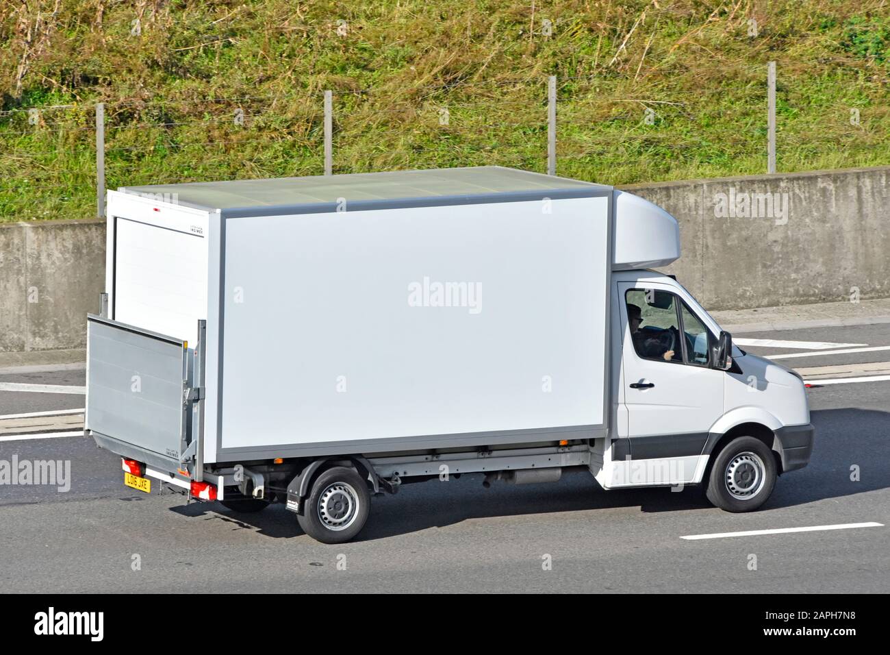 View from above side & back of white delivery van fitted with tailgate hoist for loading & unloading driver motoring along m25 motorway England UK Stock Photo