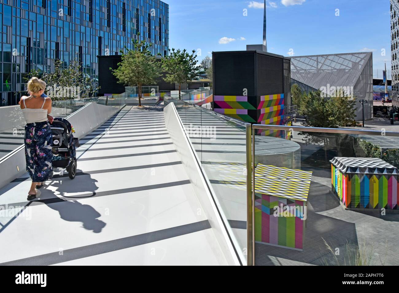 Back view of mother with baby & pushchair walking on “The Tide” high level linear park elevated walks at Greenwich Peninsula South London England UK Stock Photo