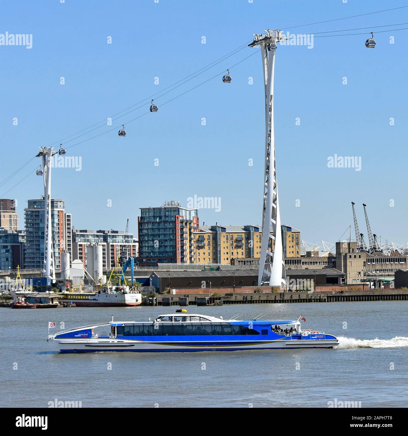 Tfl thames clipper catamaran riverbus passing below Emirates Air Line cable car link from Greenwich Peninsula to Royal Victoria Dock London England UK Stock Photo
