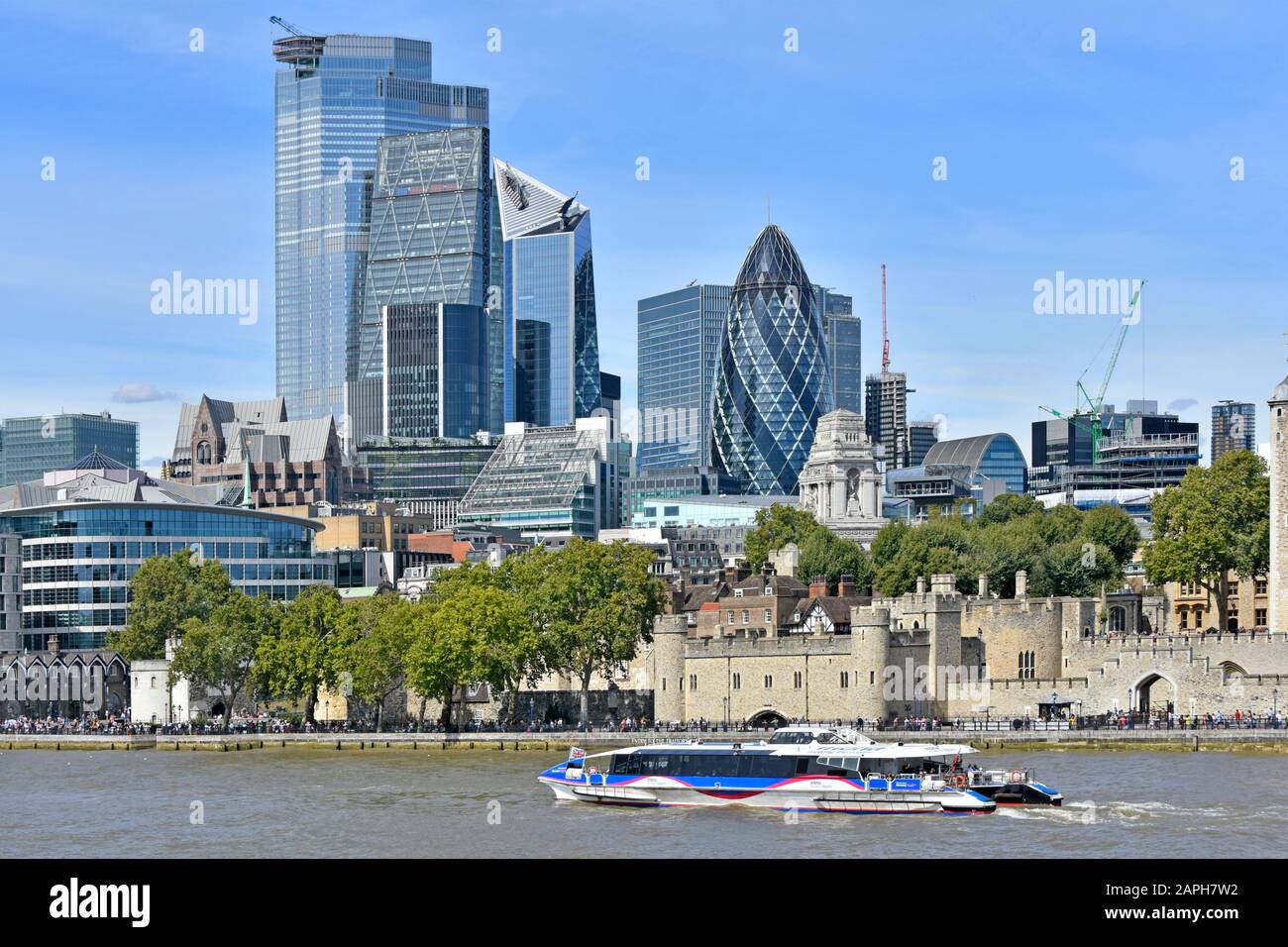 Thames clipper catamaran river bus boat on famous waterway passing historical riverside Tower of London castle & skyscraper city skyline England UK Stock Photo