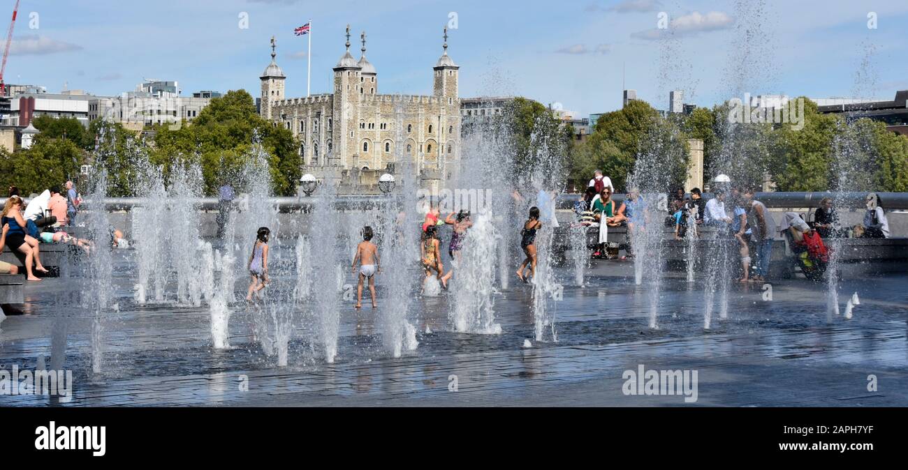 Panoramic of children playing in variable height water fountain jets hot summer weather for kids play outdoors Tower of London & White Tower beyond UK Stock Photo