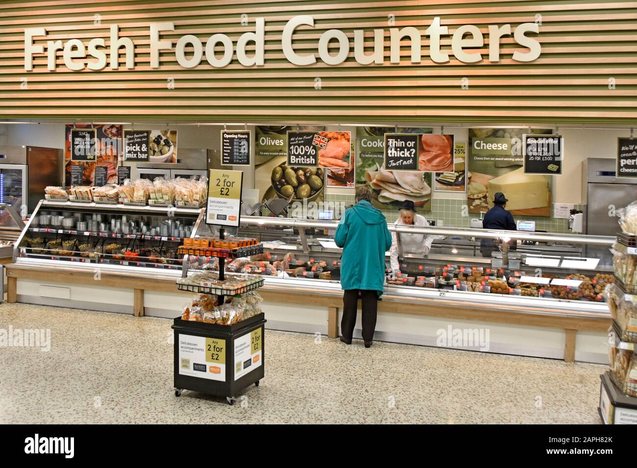 Tesco Extra supermarket store interior Fresh Food Counter back view woman shopper customer being served meat products early morning London England UK Stock Photo