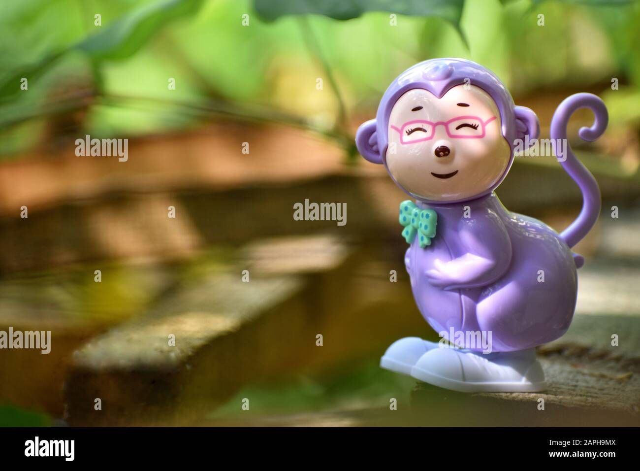 Portrait of a smiling monkey toy with greenish background and blurred leafs Stock Photo