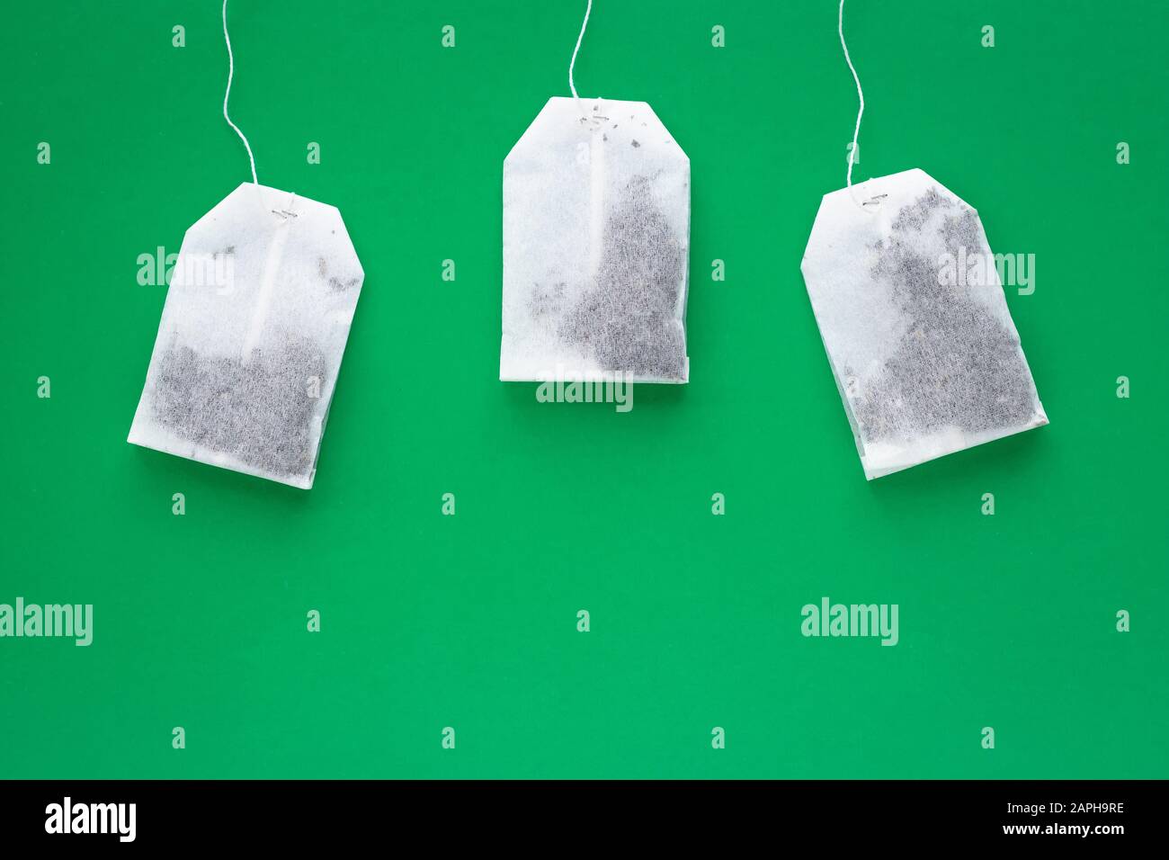Three white tea bag on green background with copy space Stock Photo