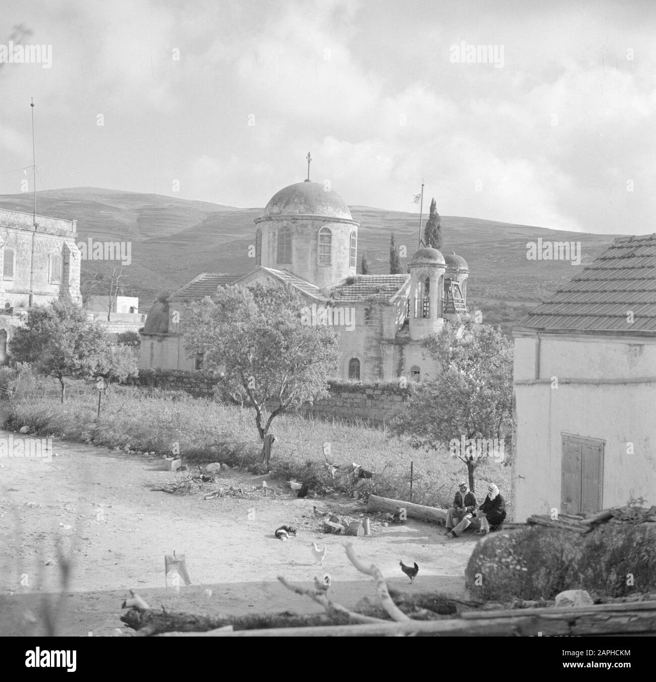 Israel 1948-1949: Kana Description: The Greek Orthodox Wedding Church in Cana, with in the foreground two villagers surrounded by scurrying chickens Annotation: The term Wedding Church refers to the miracle that Jesus of Nazareth, turning water into wine during the wedding of Cana Date: 1948 Location: Israel, Cana Keywords: village statues, church buildings, chickens, towers Stock Photo