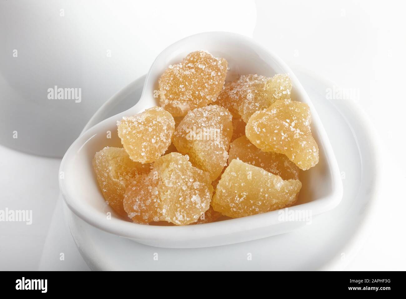 studio shot of sliced ginger cubes sprinkled with sugar in a heart-shaped cup on other white bowls Stock Photo