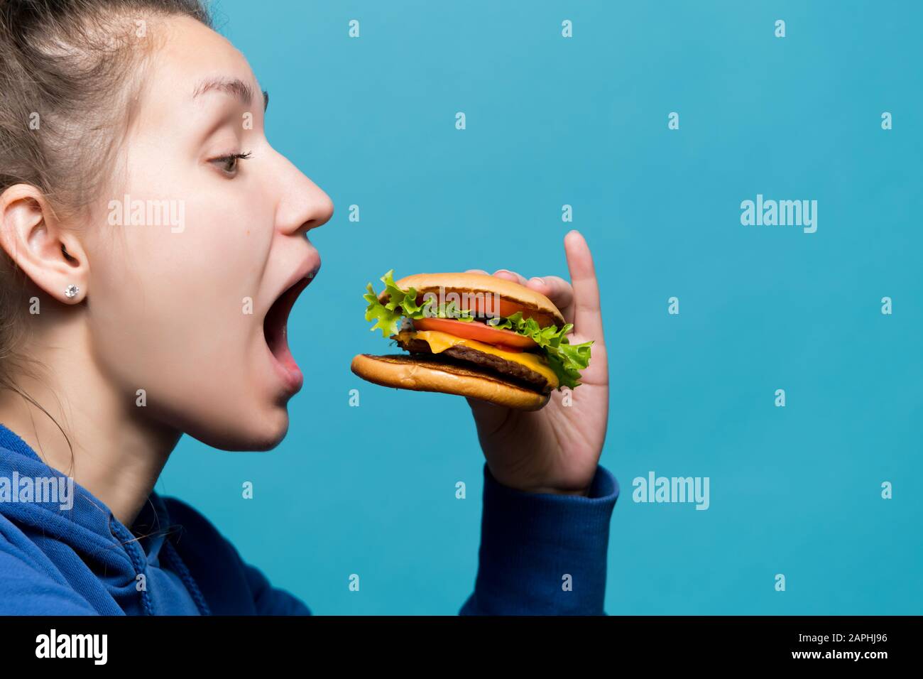 The girl opened her mouth wide and is going to eat a burger, side view Stock Photo