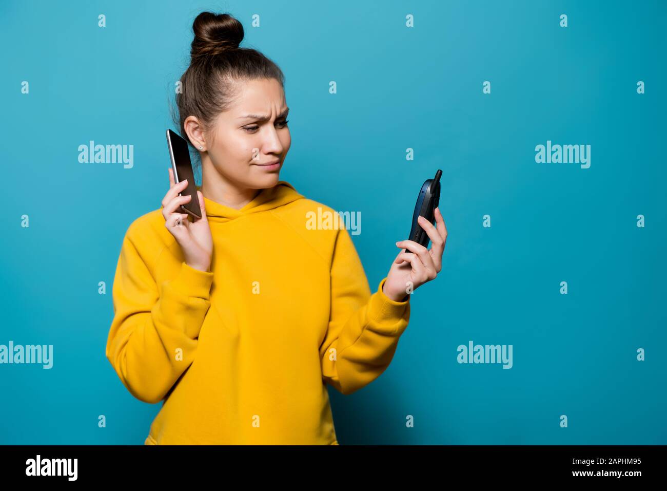 young woman puts a smartphone to her ear and looks at the old push-button telephone with slight indignation Stock Photo