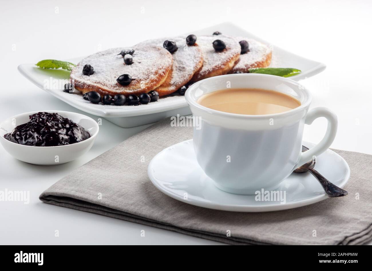 A Cup of coffee with milk and a plate with a pancakes is on the table. Stock Photo