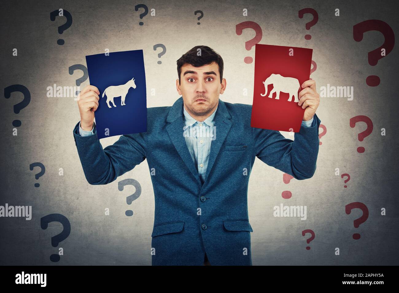 Undecided young man holding two brochures has to choose between donkeys and elephants. Perplexed and confused person with question marks around head. Stock Photo