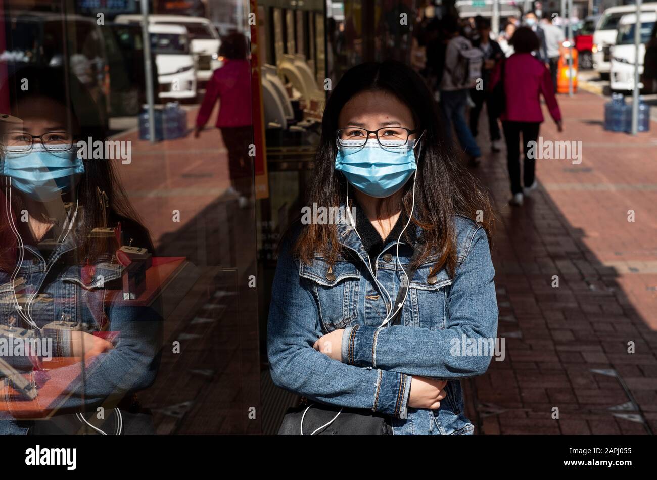 A pedestrian covers her face with a  sanitary mask after the first cases of coronavirus have been confirmed in Hong Kong. China has implemented a public transportation and airport lock down into different cities to slow down the spread of the Wuhan coronavirus. Stock Photo