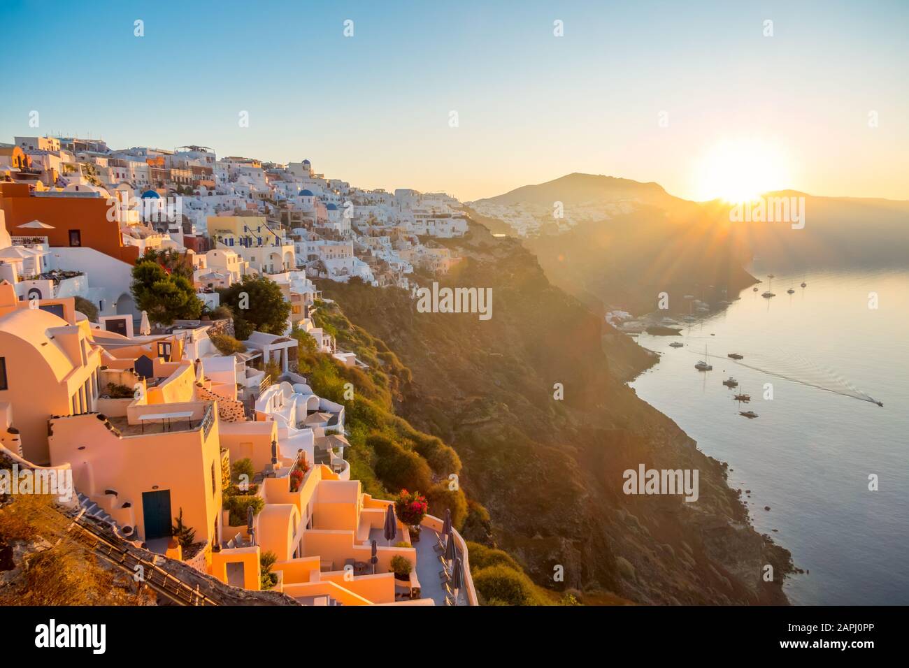 Greece. Volcanic island of Thira (Santorini). Cloudless dawn over the caldera. Many white houses of Oia city on the side of a mountain and a yacht in Stock Photo