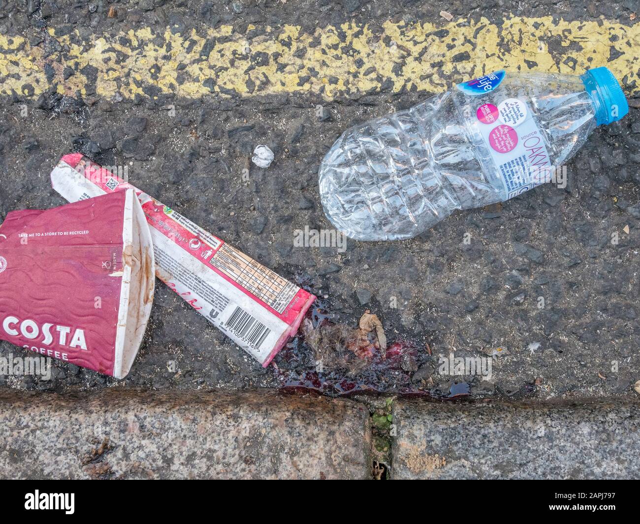 Discarded empty plastic bottle and takeaway packaging lying in London street gutter. For war on plastic, plastic pollution UK, urban street rubbish. Stock Photo