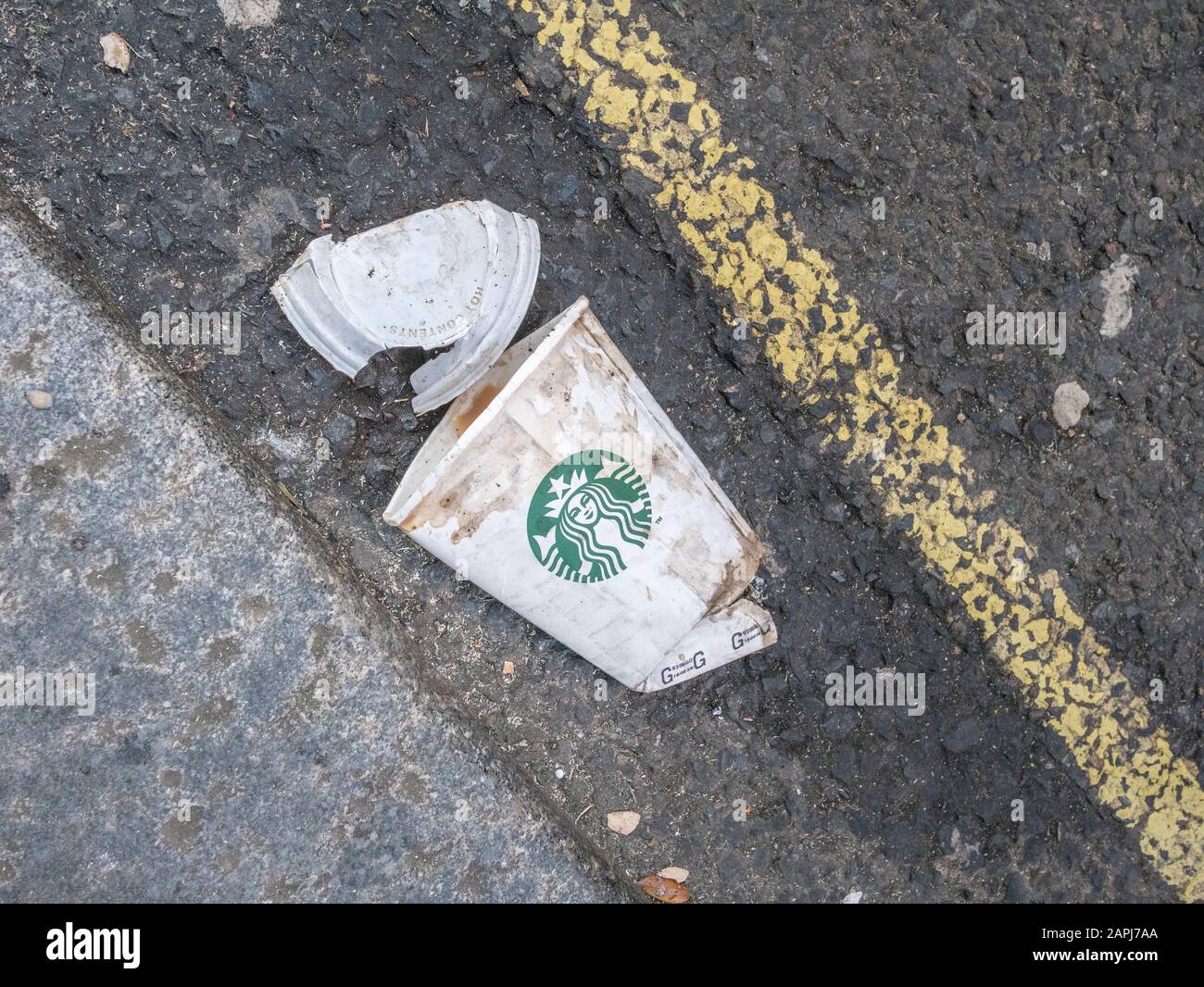 Crushed Starbucks takeaway coffee cup (paper) with plastic lid in London street gutter. For takeaway food packaging, plastic litter, urban rubbish. Stock Photo