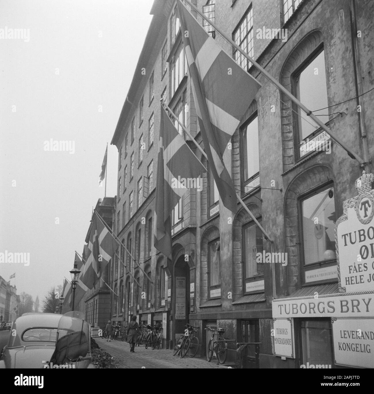 55th anniversary of King Frederick IX Description: Danish flags at the Tuborg Brewery in honor of the King's birthday Date: March 11, 1954 Location: Denmark, Copenhagen Keywords: Cars, breweries, bicycles, street images, birthdays, flags Stock Photo
