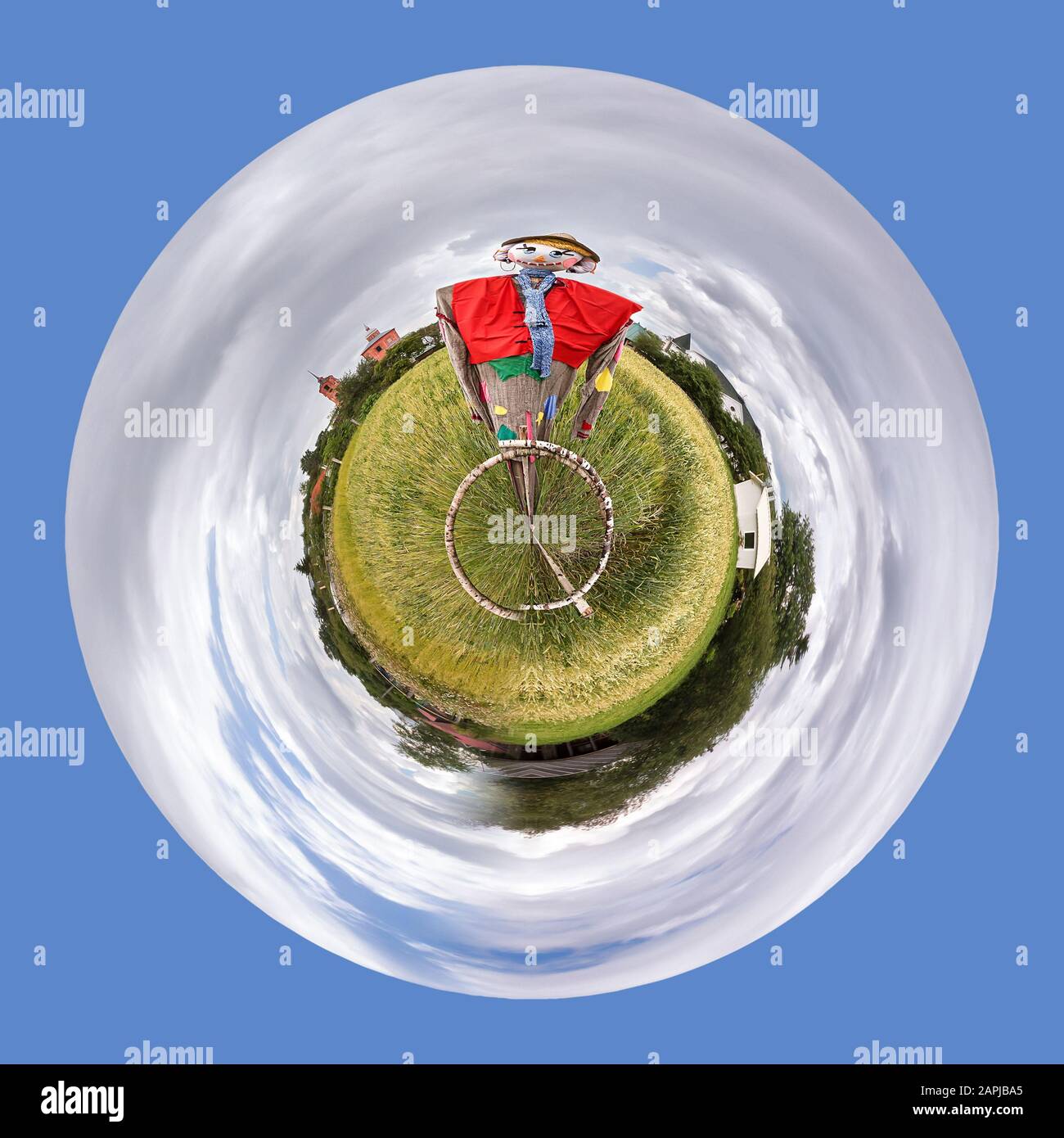 Abstract planet with a field and a Scarecrow, surrounded by blue sky and clouds. Stock Photo