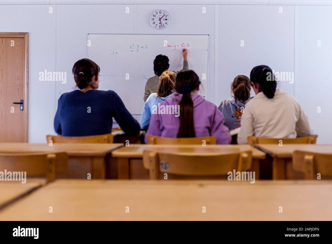 Pupils in classroom from behind with teacher writing on whiteboard Stock Photo