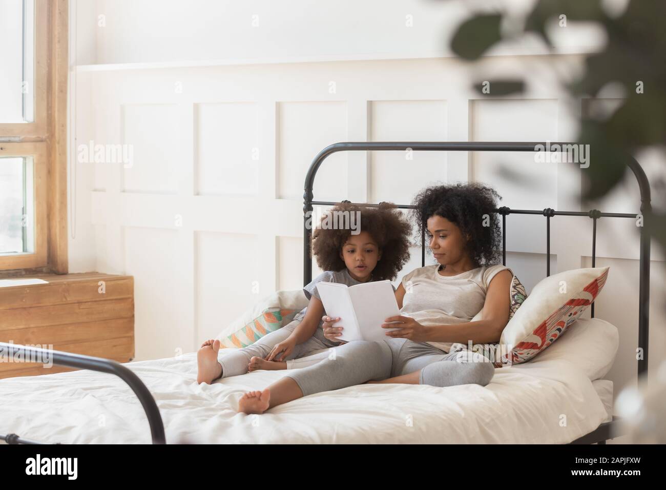 Lying in bed african mother reading bedtime book to daughter Stock Photo