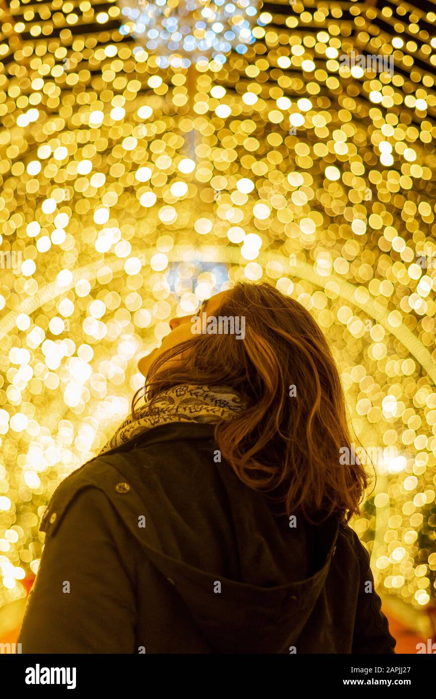Girl seen from behind looking up with christmas lights in the background Stock Photo