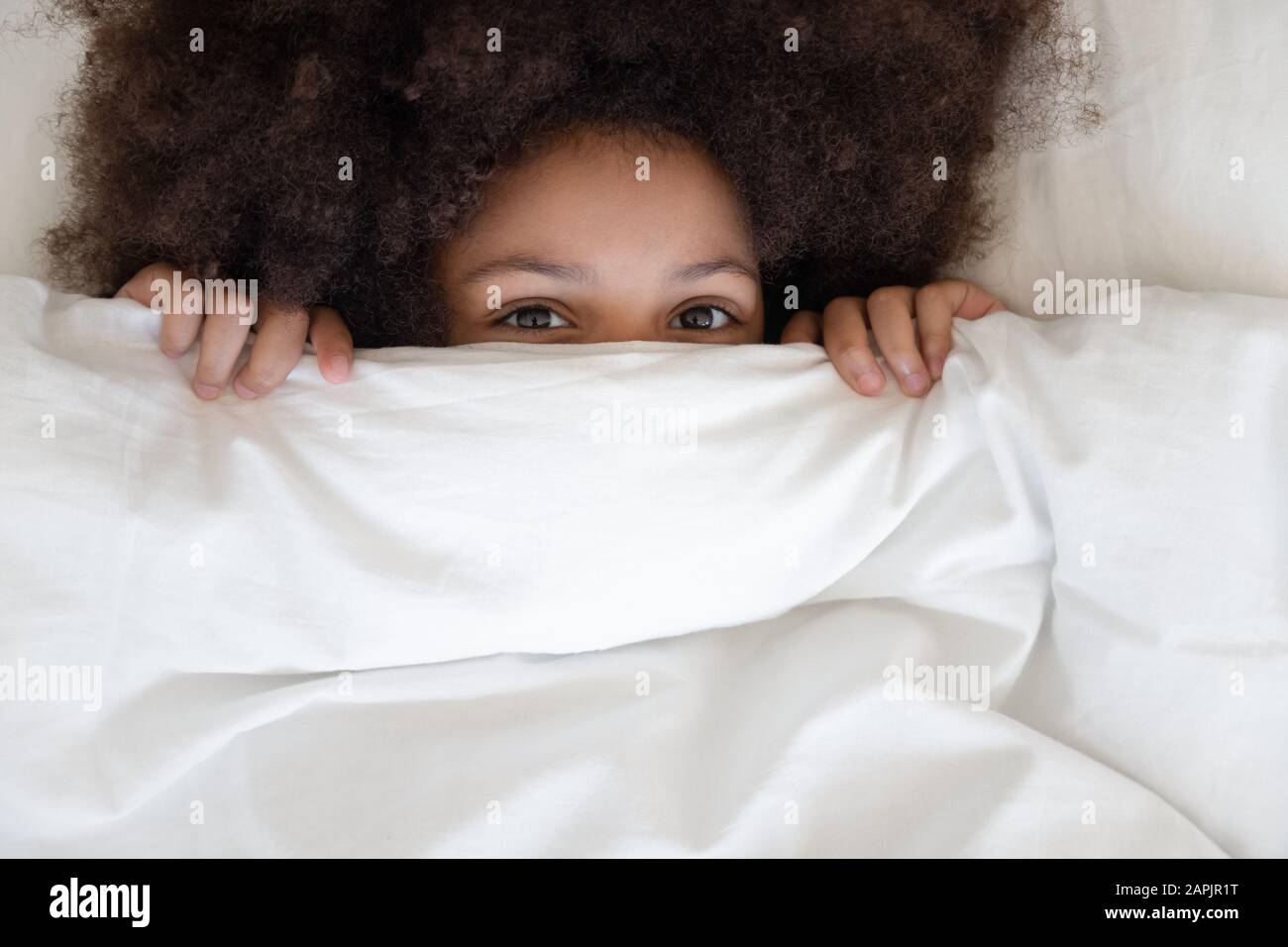 Cute little african girl hides behind blanket looking at camera Stock Photo