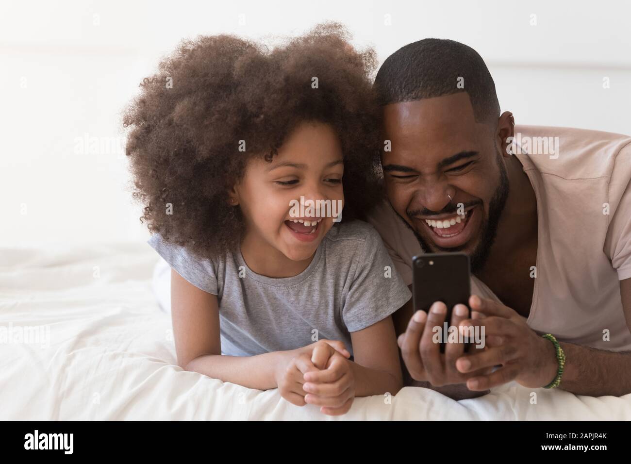 Dad and daughter lying in bed having fun using smartphone Stock Photo -  Alamy